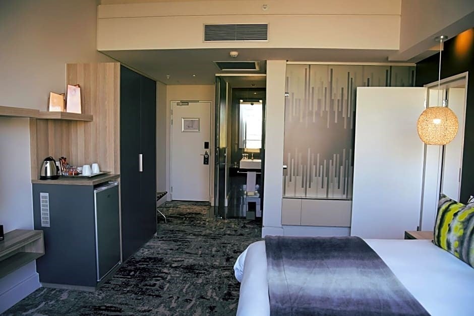 Modern hotel room with a bed, decorative pillows, abstract artwork, bedside lamp, and visible bathroom area. Modern hotel room with a bed, decorative pillows, abstract artwork, bedside lamp, and visible bathroom area.