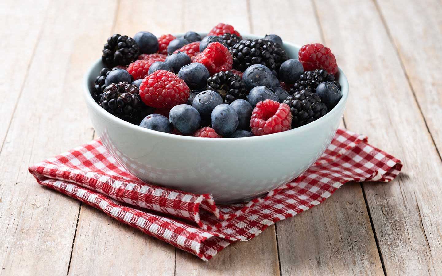 A bowl of mixed fresh berries on a red and white checkered cloth.