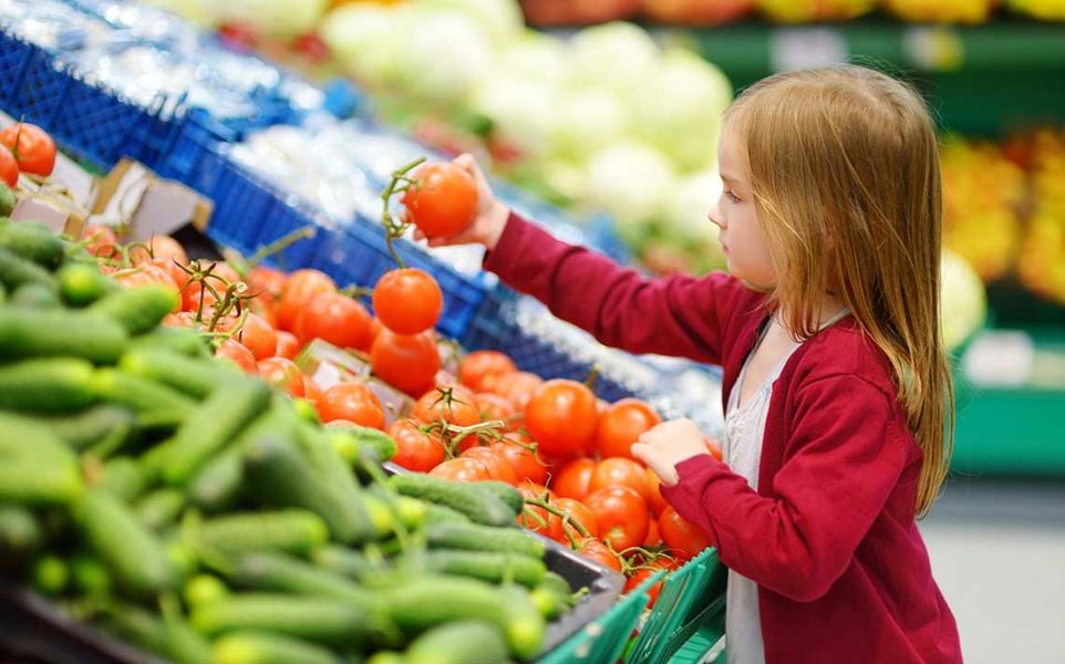 Child selecting tomatoes in a supermarket produce section.