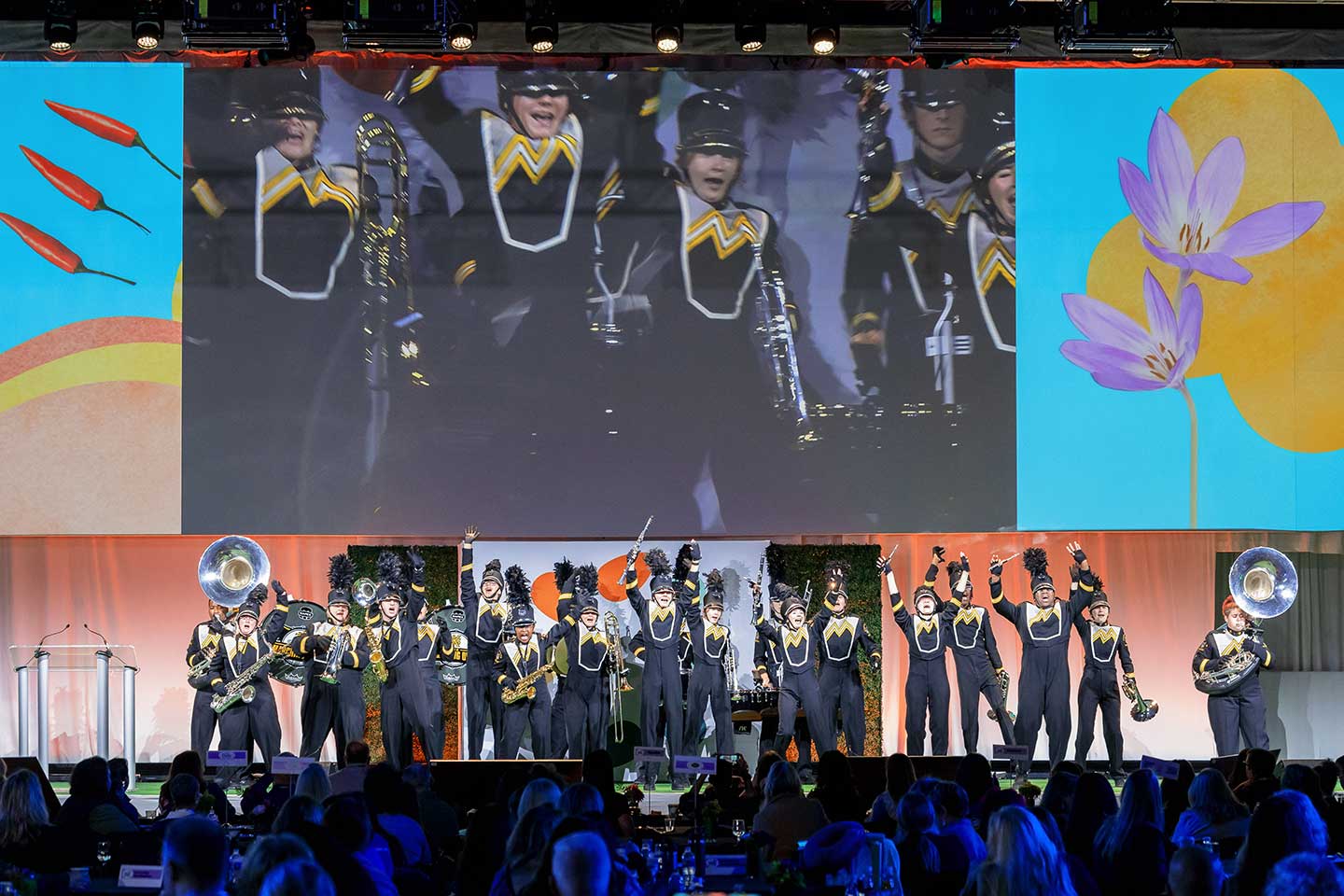 A marching band performing on stage at the Global Produce and Floral show with large screen and colorful graphics in the background. A marching band performing on stage at the Global Produce and Floral show with large screen and colorful graphics in the background.
