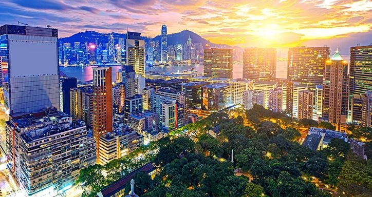 Tsim Sha Tsui Hong Kong at sunset with skyscrapers, a park, and a body of water reflecting city lights.