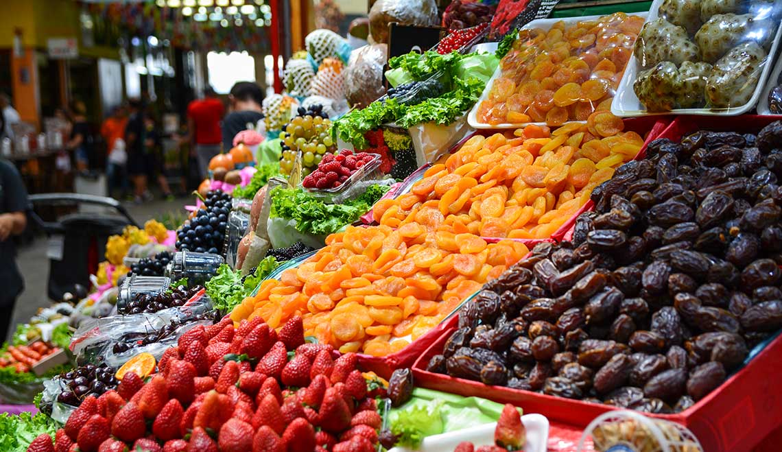 A market stall filled with colorful fruits, including dried apricots, dates, strawberries, and blackberries.
