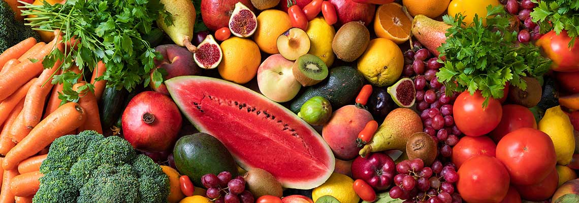 Assorted fresh fruits and vegetables, including watermelon, carrots, broccoli, figs, citrus fruits, apples, grapes, and parsley.