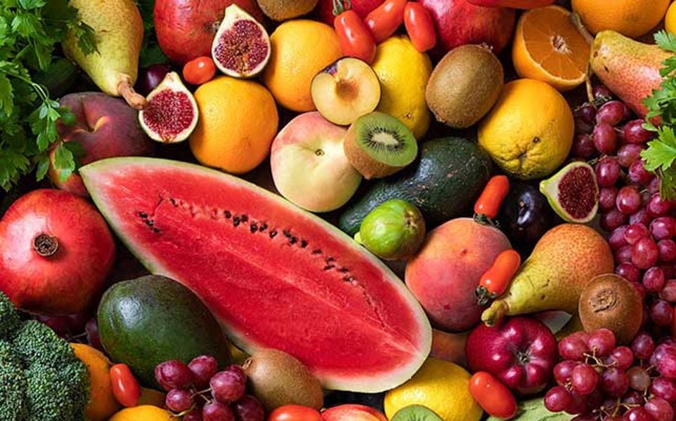 Assorted fresh fruits and vegetables, including watermelon, carrots, broccoli, figs, citrus fruits, apples, grapes, and parsley.