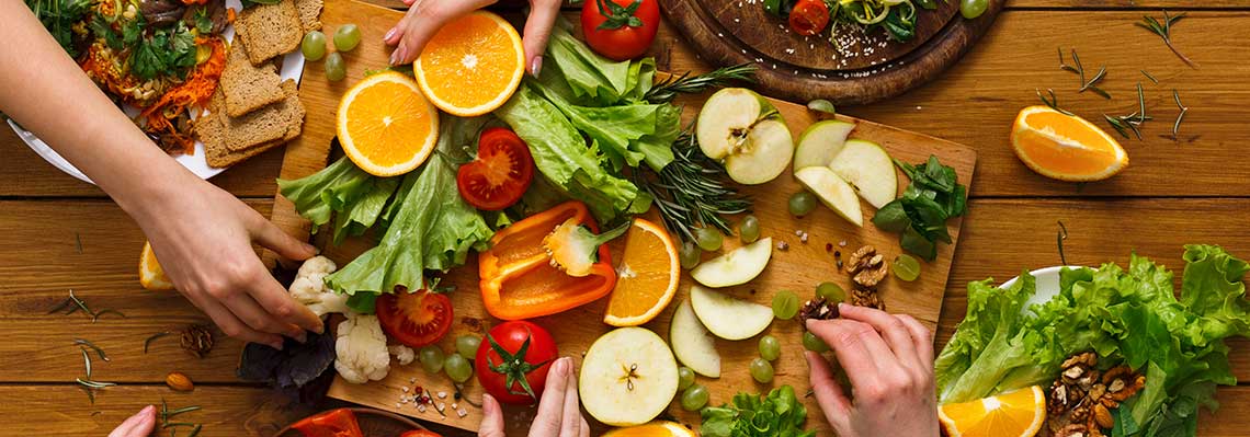 Assorted colorful fruits and vegetables, including a sliced watermelon, carrots, tomatoes, broccoli, grapes, and more.