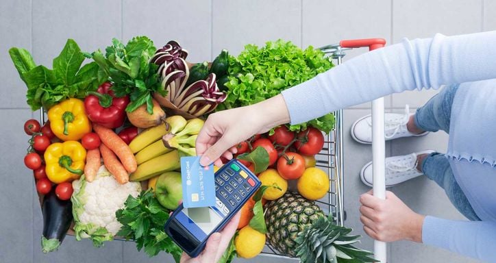 Woman pushing a shopping cart full of fresh vegetables and fruits, she is holding a delicious apple, top view