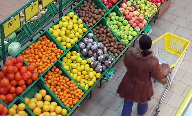 A view from above as a female shopper pushes a grocery cart surrounded by displays of fruits and vegetables.
