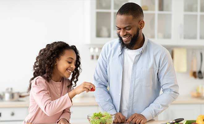 A father and daughter prepare a meal together in their kitchen.