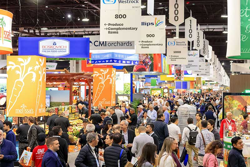 Global Produce and Floral Show scene with numerous attendees browsing produce booths under signs indicating different sections.
