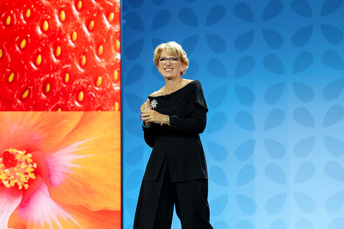 Woman on stage with large images of a strawberry and a flower in the background.