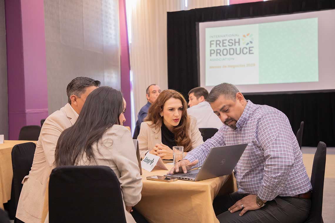 A group of four people engaged in discussion around a table with a laptop, during a professional event.