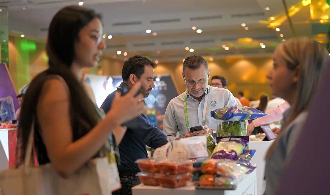 People interacting near a display of fresh produce in a brightly lit indoor venue.