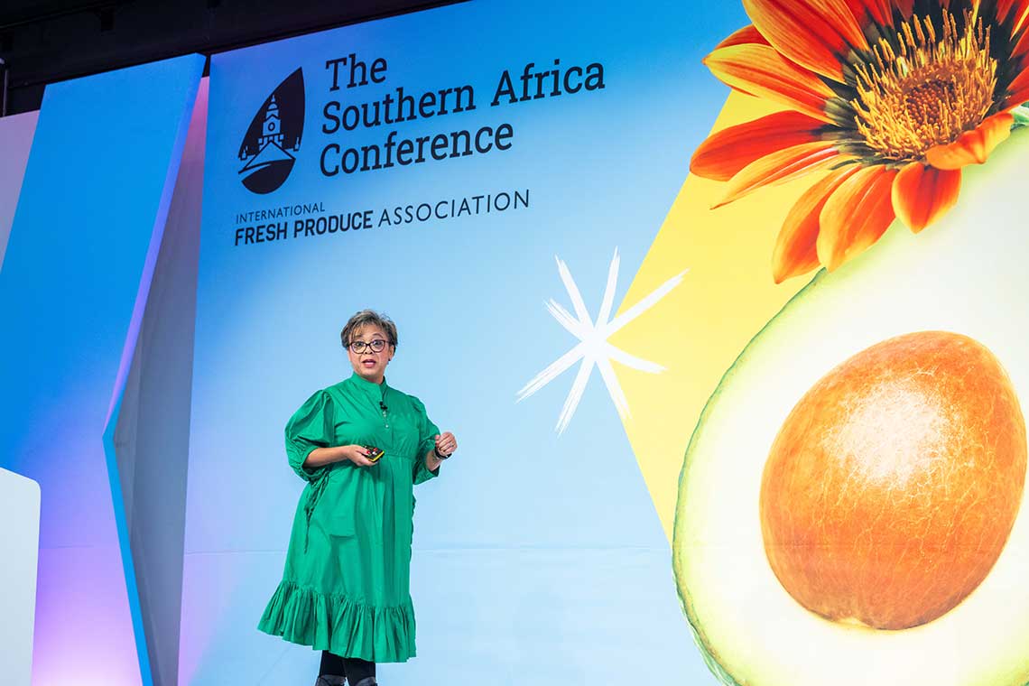 A speaker at The Southern Africa Conference by IFPA, standing in front of a colorful banner featuring a flower and avocado.