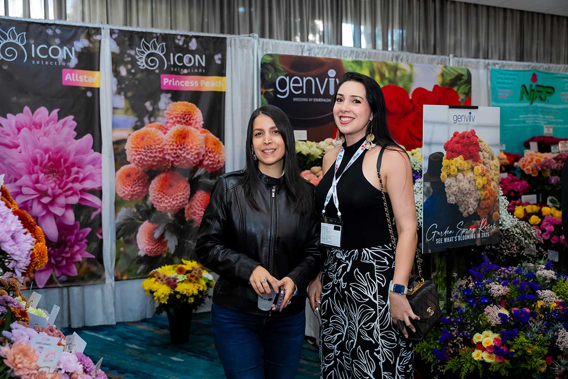 Two women at a flower exhibition with colorful flower displays and banners in the background.