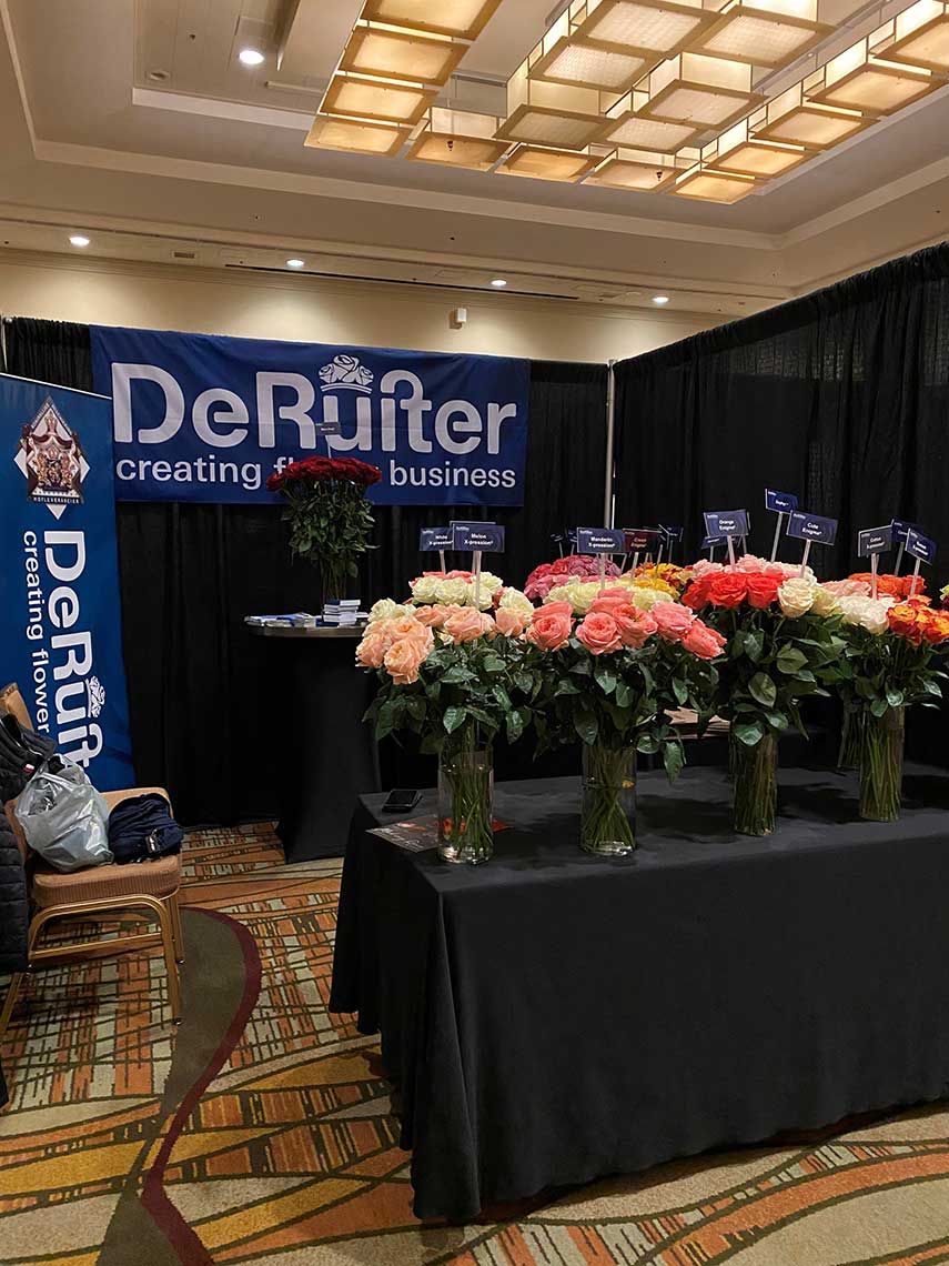 A trade show booth displaying roses in vases and a banner reading "De Ruiter creating flower business."