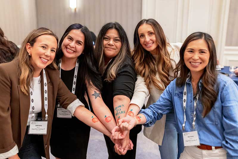 Five women at the IFPA Women’s Fresh Perspectives Conference smile together with their hands joined in the center.