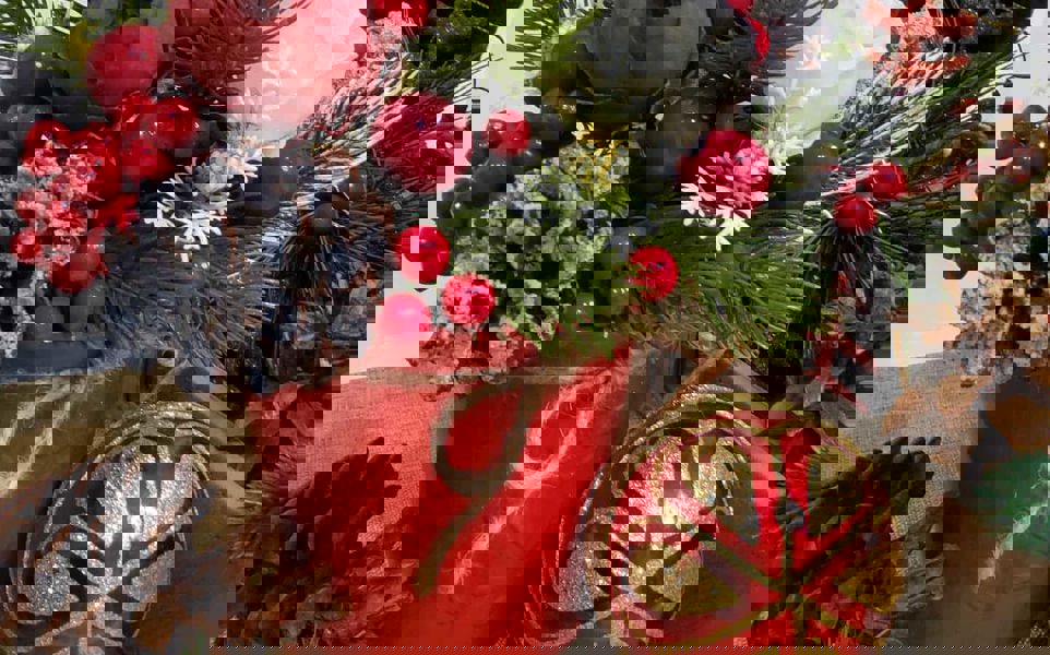 Festive Christmas arrangement with pine branches, berries, flowers, and decorations in a red pot.