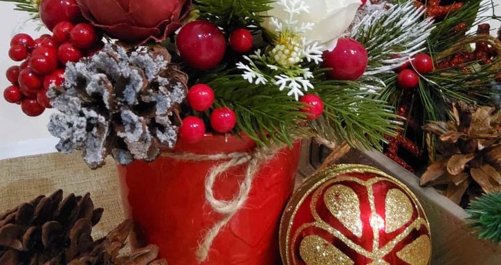 Festive Christmas arrangement with pine branches, berries, flowers, and decorations in a red pot.