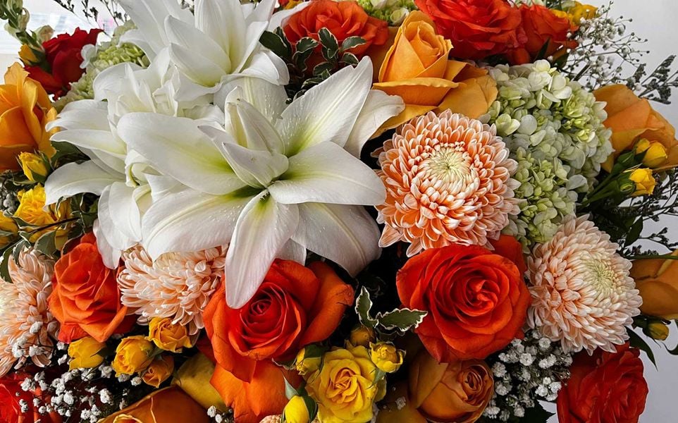 A colorful bouquet featuring white lilies, orange roses, yellow rosebuds, and orange and white chrysanthemums.