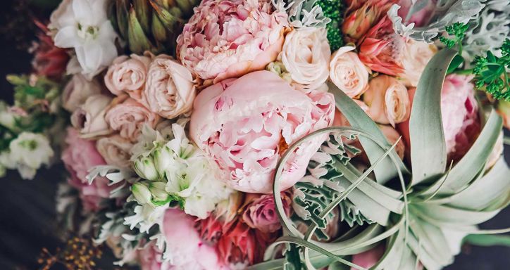A close-up of a bouquet featuring pink peonies, cream roses, white flowers, and green foliage.