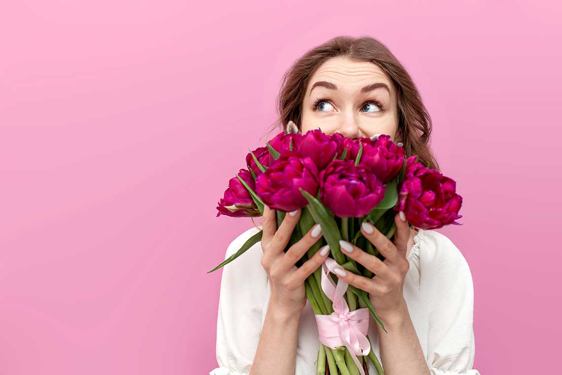 Person holding a bouquet of pink peonies against a pink background.