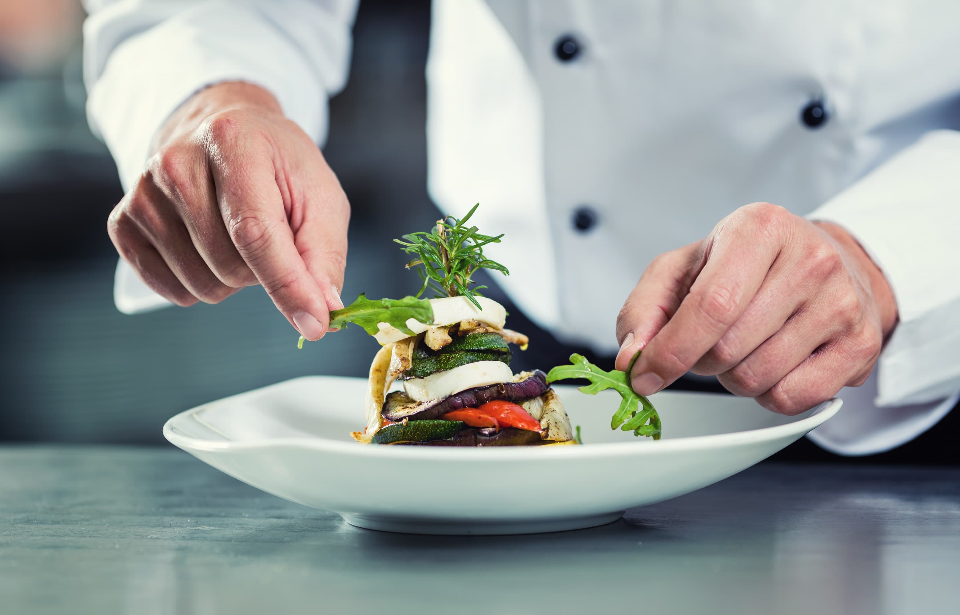 Chefs hand garnishing plate with stacked vegetables Chefs hand garnishing plate with stacked vegetables