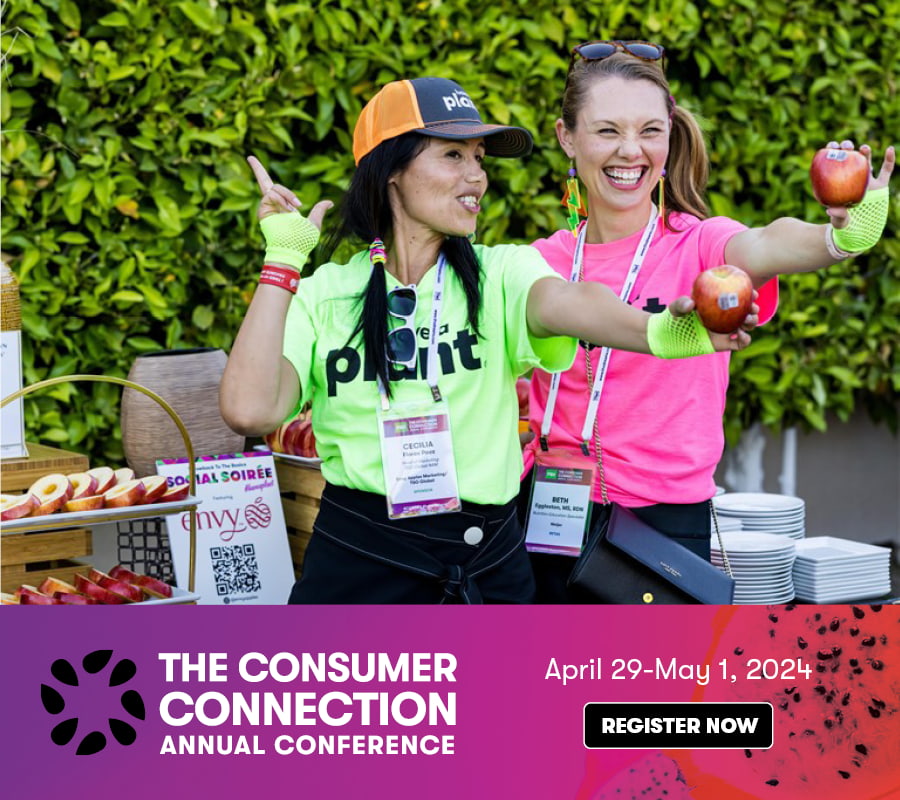 Two smiling women wearing brightly colored shirts holding apples with conference lanyards around their necks. The text says: The Consumer Connection Annual Conference April 29 - May 1, 2024 Register now