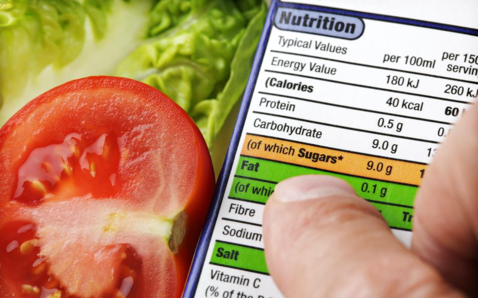 Hand holding a nutrition label next to salad with tomato and romaine lettuce