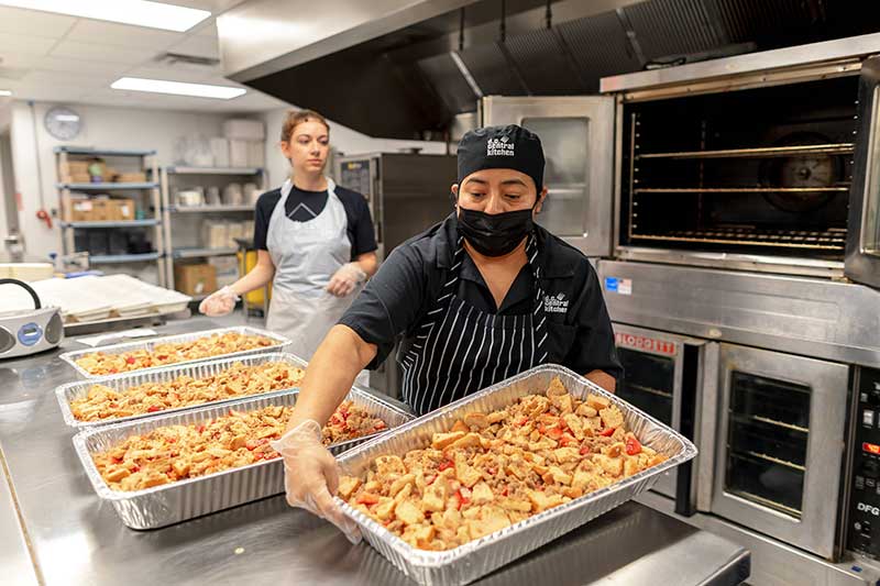 A group of women from DC Central Kitchen prepare strawberry French toast in a school cafeteria kitchen.