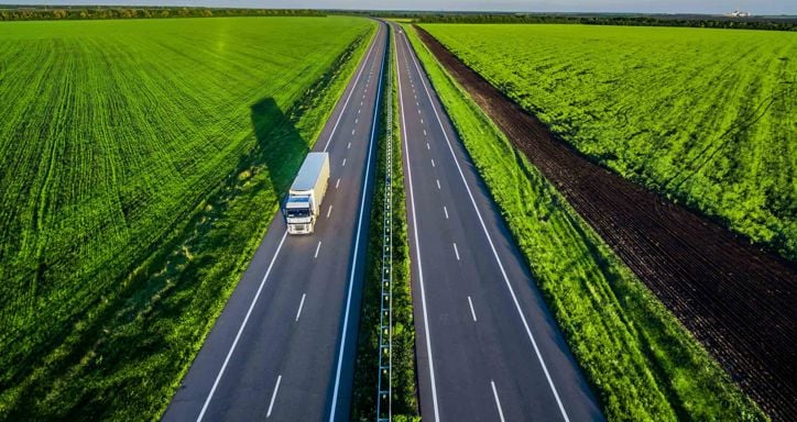 White trucks driving on asphalt road along the green fields in rural landscape. 