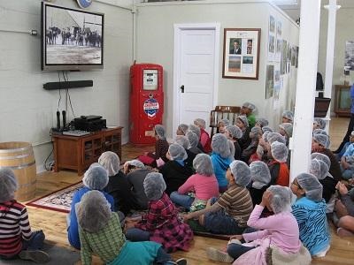 Group of school children wearing hairnets sit cross legged on the floor watching TV