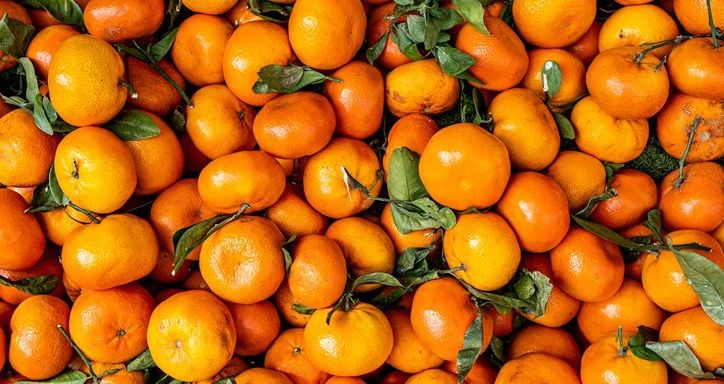 A pile of ripe clementines with some green leaves attached.