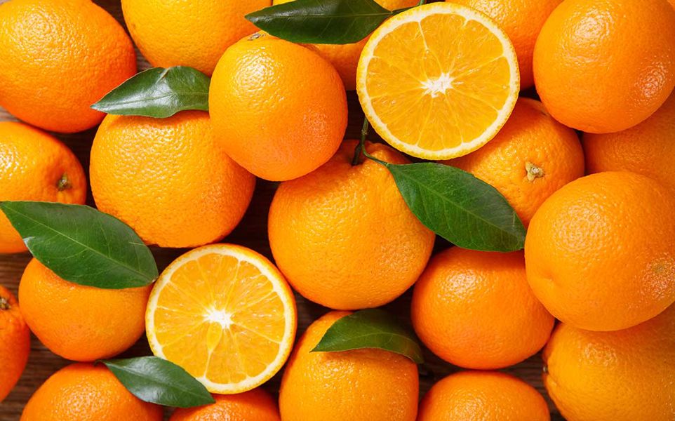 A pile of fresh oranges with two cut in half, showing the interior, and some green leaves scattered among them.