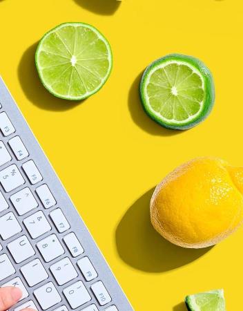 Yellow table covered with limes and lemons and two hands on a wireless computer keyboard