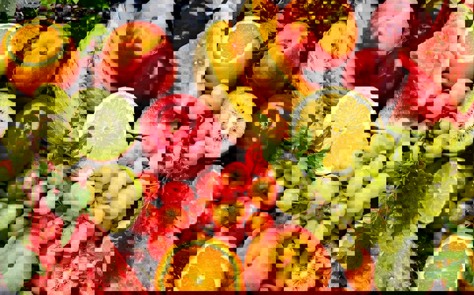 Assorted fresh fruits including grapes, apple, peaches, watermelon and more on dark background.