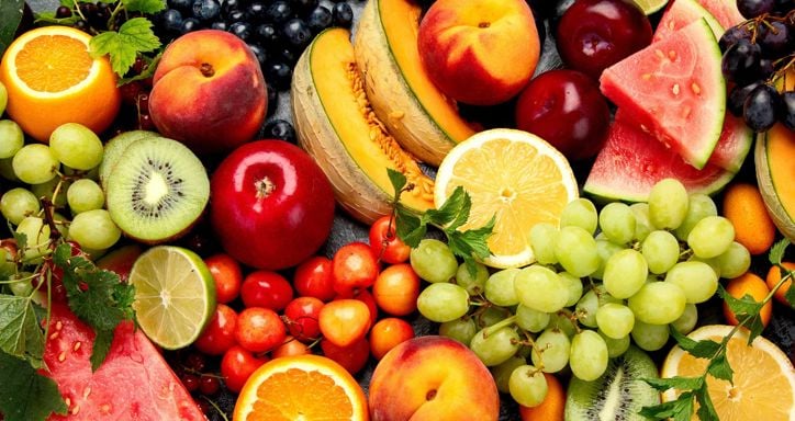 Assorted fresh fruits including grapes, apple, peaches, watermelon and more on dark background.
