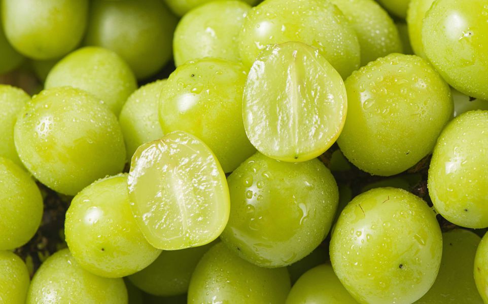 A macro image of green table grapes. One of the grapes is cut in half.