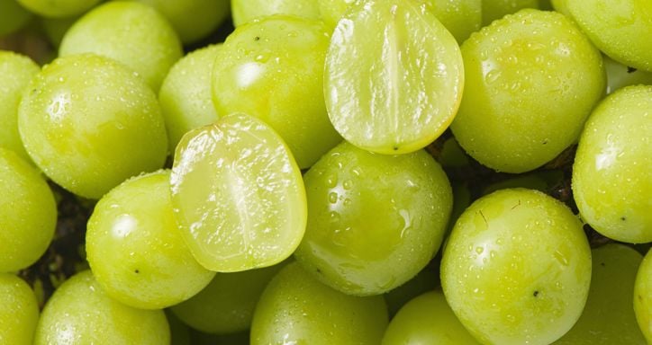 A macro image of green table grapes. One of the grapes is cut in half.