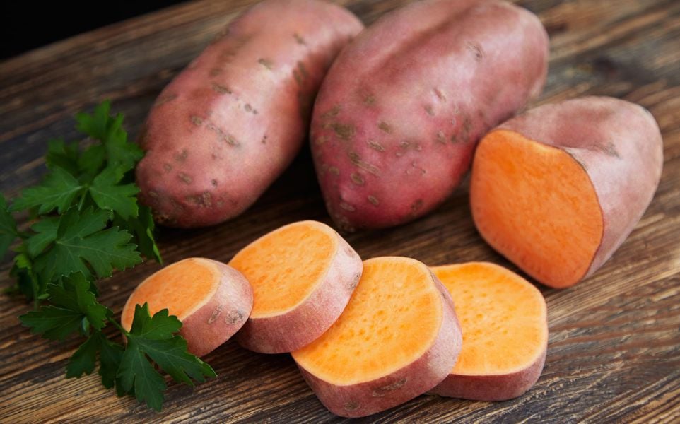 Raw sweet potatoes on a rustic wooden table decorated with parsley.