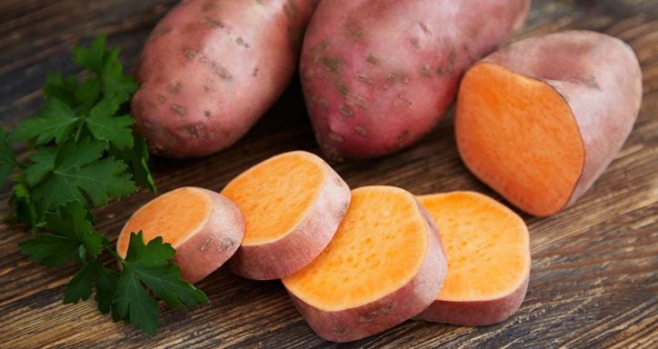 Raw sweet potatoes on a rustic wooden table decorated with parsley.