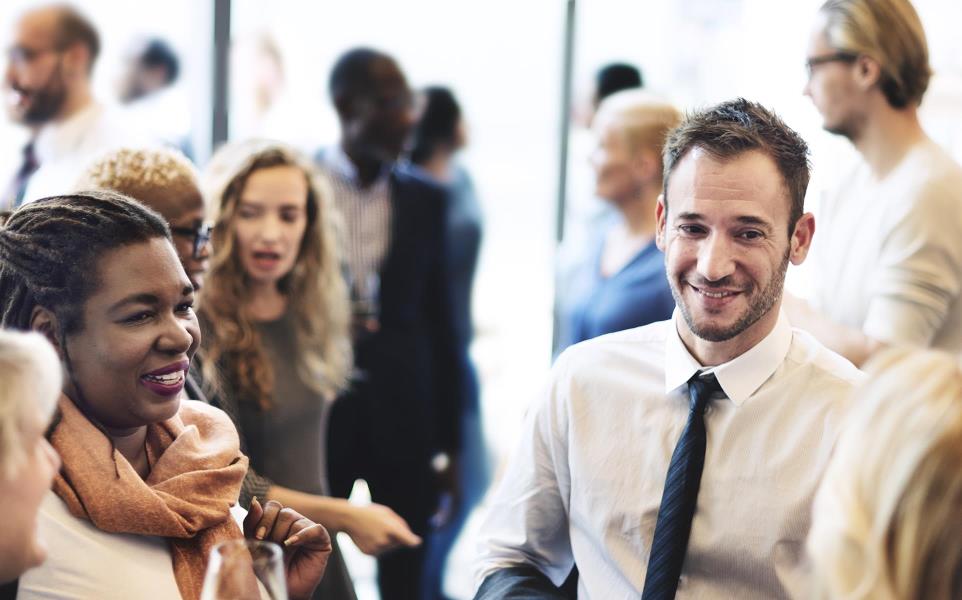 Diverse group of males and females dressed in business attire chatting at a gathering while drinking wine