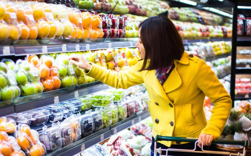 Young woman browsing the produce aisle with her shopping cart