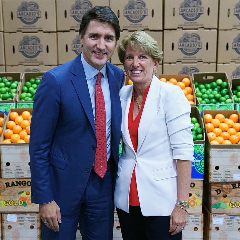 Canadian Prime Minister Justin Trudeau and IFPA CEO Cathy Burns pose for a picture in front of a display of open boxes of fruit.