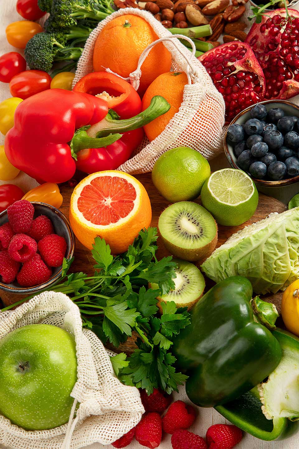 An assortment of fruits and vegetables, including a sliced orange, bell peppers, tomatoes, and berries, arranged on a wooden surface.